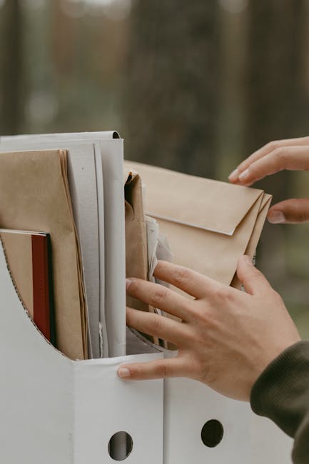 Popieriniai dokumentai ir dėžutė ant stalo prieš nuskenuojant į archyvą