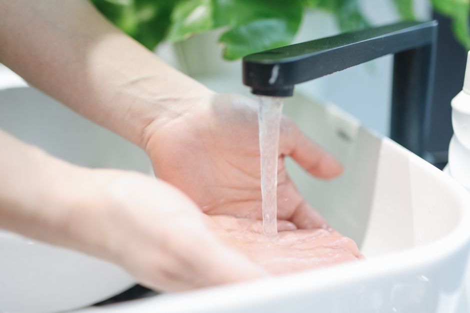 Žmogus prie karšto vandens čiaupo laukia, kol taps tinkamos temperatūros